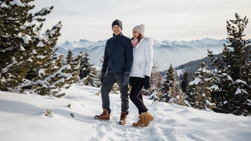 Couple wearing insulated winter hiking pants in the snow, demonstrating What pants are best for cold weather during a mountain winter adventure.
