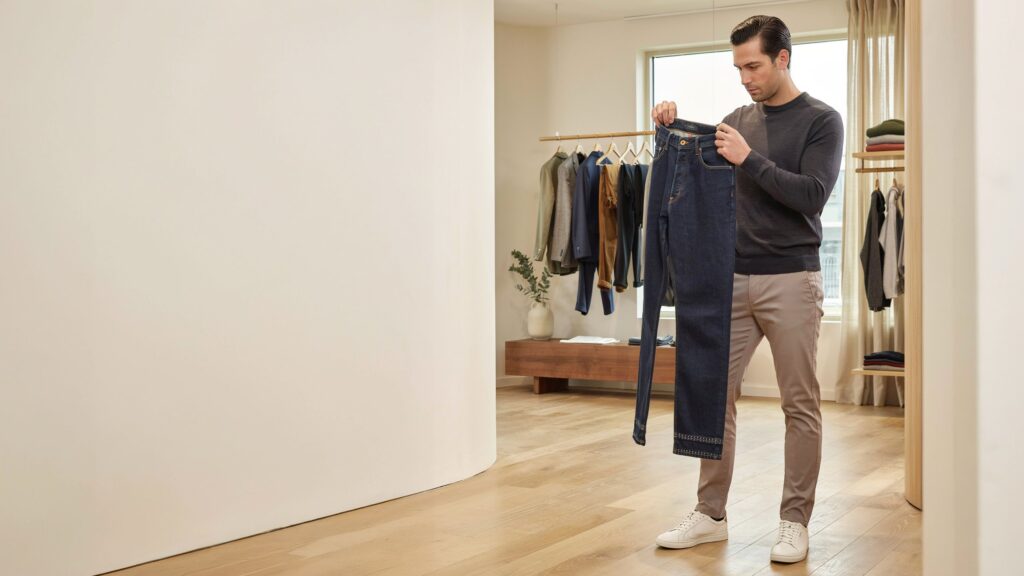 Signs of good-quality pants – man inspecting a pair of dark denim pants to check fabric quality, stitching, fit, durability, and overall craftsmanship before buying.